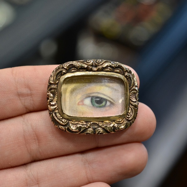 A Late 18th Century Gold Mounted “Lover’s Eye” Miniature Brooch #bernardo 

The rectangular brooch centred with a glazed compartment depicting a painted miniature of a lady’s eye, frame with rocailles, approx. 3.5 x 2.8 cm, approx. 11.5 g

One curious type of miniature was the “Lover’s Eye”, a subgenre of jewelry that was very popular during the Georgian era. For centuries, small personal portraits of a loved one had been common adornments in the costume of the time, but representations of that person’s eyes were something truly new. Wealthy people wore these charms on everything from rings to brooches to, of course, pendants. Lover’s eyes, often set in ivory plaques, were graceful and discreet. Presumably, only the wearer and the sitter knew the identity of the depicted lover, making the experience totally intimate and mysterious. The Prince of Wales is said to have given his wife, Mary Fitzherbert, a miniature of his right eye, they later separated, but when he died in 1830, they discovered that he was wearing a necklace with a padlock pendant near his heart with Fitzherbert’s eye inside. The places on the body where people wore them (on the wrist or near the heart) created a tactile and emotional connection that reflected the sentimental closeness between the subject and the wearer.