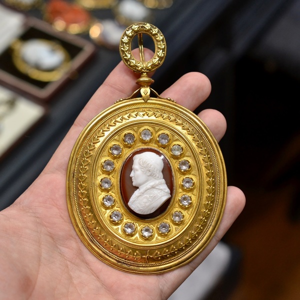 Pectoral Gold Pendant from Castellani with a Cameo Attributed to Luigi Saulini (1819-1883) Showing Pope Pio IX’s Effegy #bernardo 

Pendente in oro inciso e in filigrana attribuito a Castellani, con al centro un cammeo in agata raffigurante Sua Santità Papa Pio IX, circondato da una fila di pietre incolore e ghirlande stilizzate a rilievo, reca sul retro inciso lo stemma della famiglia Mastai Ferretti a cui apparteneva sua Santità, mm 90X68, gr 105. Corredato di cartiglio in cui viene riportato come segue: “regalato da S. Santità Pio IX alla Contessa Giulia Guicciardini Pucci, nell’occasione della sosta che fece Santità Sua il 18 Agosto 1857 nella Villa Guicciardini a Montughi.”
L’angelico Pio IX è finalmente in mezzo a noi, fra le mura della bella Firenze, e nella capitale della gentile Toscana. Chi non sente il cuore inondato di gioia, l’animo ripieno di ineffabile contentezza al faustissimo avvenimento? O giorno felice in cui è dato di potere ammirare ed ossequiare il venerando Pontefice”.”
Così le cronache del tempo annunciavano la visita di Papa Pio IX a Firenze durante l’estate del 1857.
Testimonianze storiche confermano che Il 18 Agosto di quell’anno verso mezzogiorno e un quarto il corteo papale giunse a Villa Guicciardini, presso “La Pietra”, a Montughi, alle porte di Firenze. Dopo un breve riposo Pio IX pranzò con il Granduca di toscana e gli Arciduchi, col suo seguito di nobili signori.
Nelle memorie della Contessa Giulia Pucci Guicciardini, conservate nell’archivio storico Guicciardini di Poppiano (Montespertoli, Firenze), risulta che durante la sua visita presso il Castello di Poppiano, Sua Santità Papa Pio IX abbia lasciato un medaglione con pietre dure e preziose, insieme alla brocca e al bacile utilizzati per la messa (purtroppo trafugati dal palazzo di famiglia del Lungarno nel 1944, dove si conservava anche la poltrona in velluto rosso usata dal pontefice).
Please Note : the object is not available for export outside Italy.